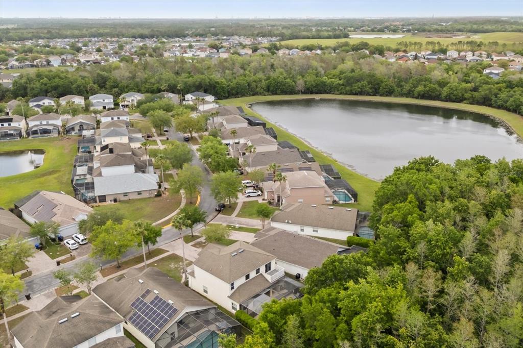 An aerial view shows a suburban neighborhood with houses, a lake, and surrounding trees — 4722 CUMBRIAN LAKES DRIVE, KISSIMMEE, FL