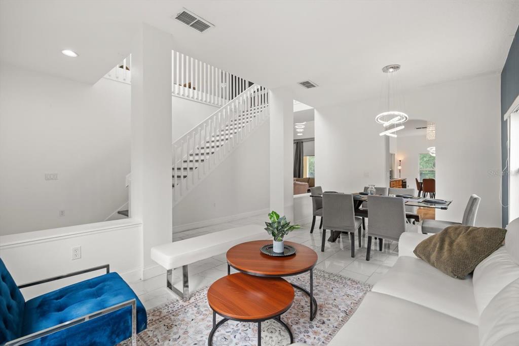 A bright living and dining area features white tile floors, a staircase, and modern furniture — 4722 CUMBRIAN LAKES DRIVE, KISSIMMEE, FL