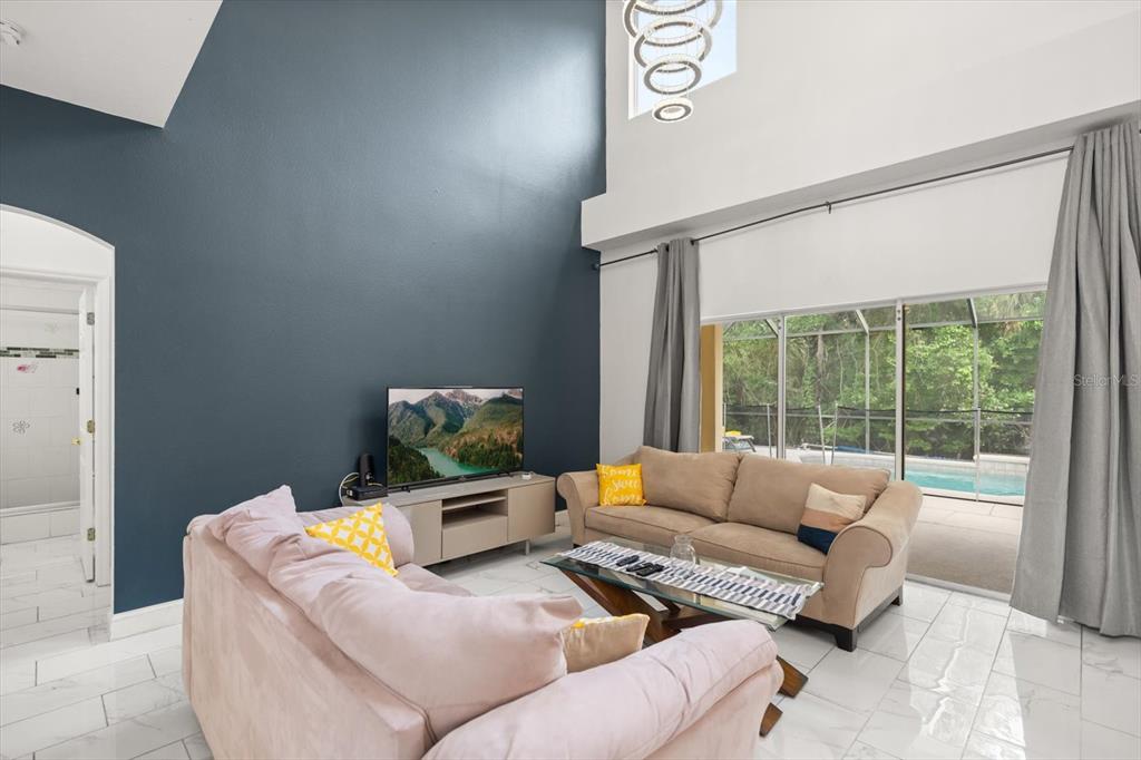 A living room features a dark accent wall, high ceilings, tile floors, and a pool view — 4722 CUMBRIAN LAKES DRIVE, KISSIMMEE, FL