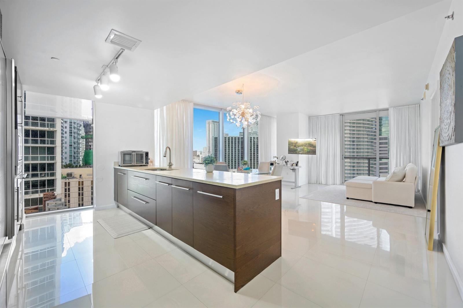 A modern kitchen with dark wood cabinetry and a white island overlooks a city skyline — 475 Brickell Avenue # 1815, Miami FL 33131, MIAMI, FL