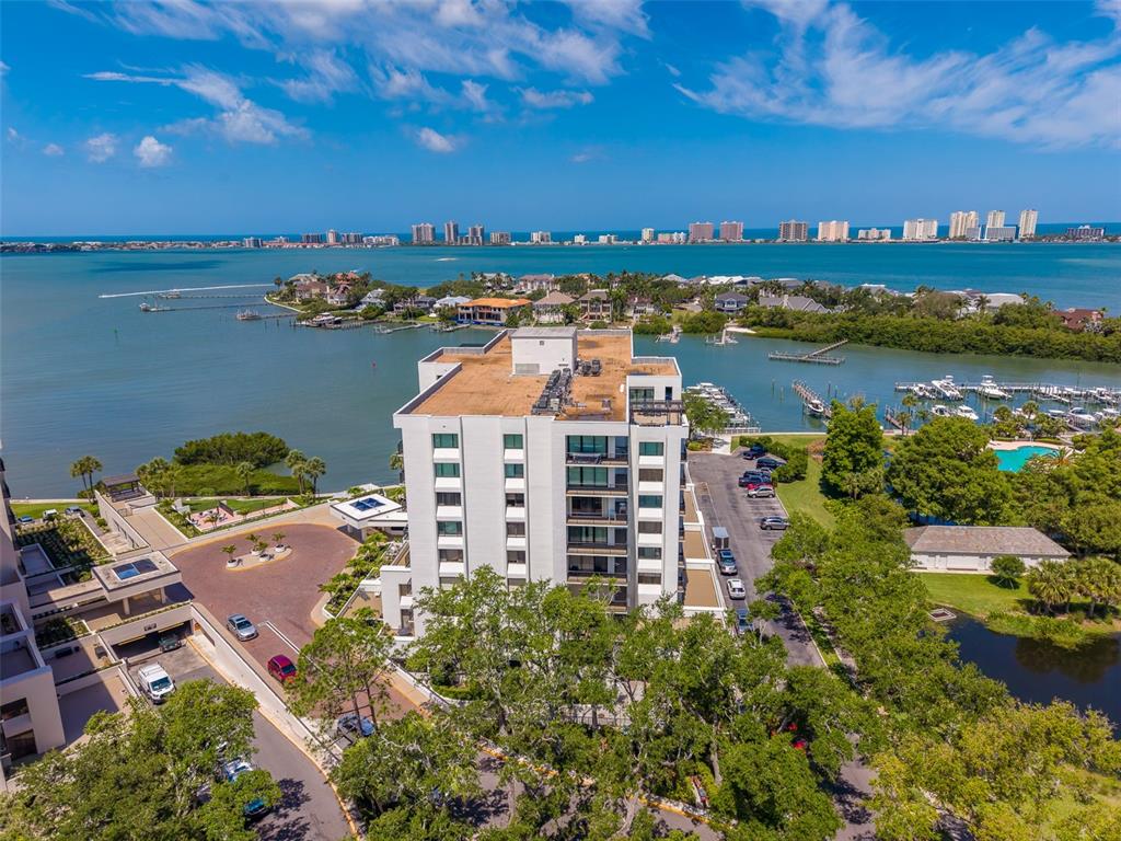 An aerial view shows a multi-story residential building surrounded by trees, parking, and waterfront docks — 8 BELLEVIEW BOULEVARD UNIT 507, BELLEAIR, FL