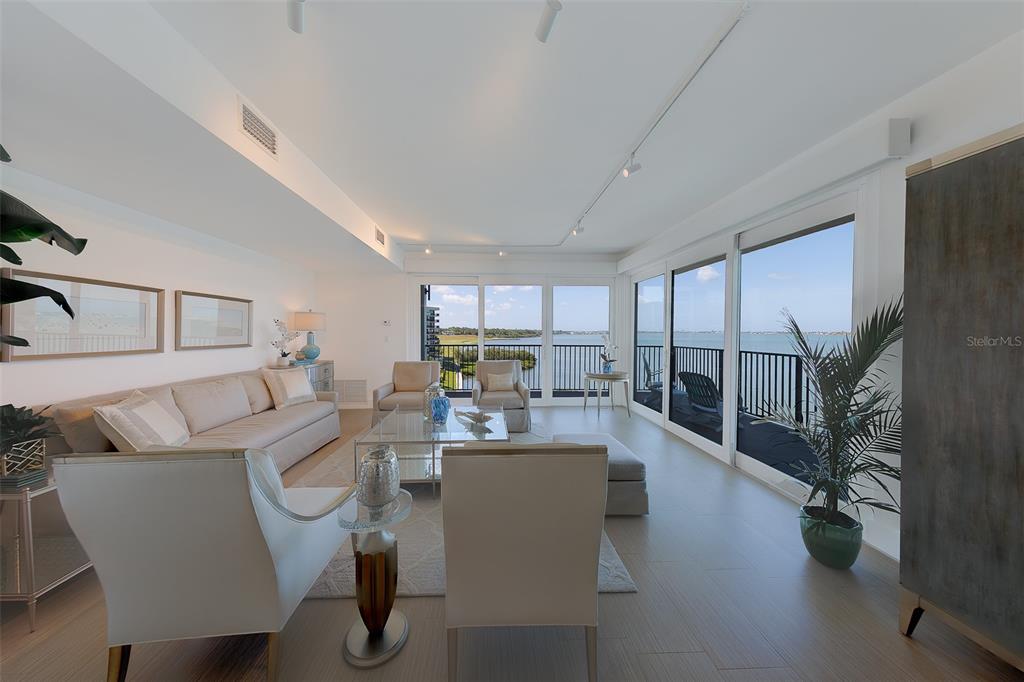 A bright living room features neutral furniture, a glass coffee table, and large balcony doors — 8 BELLEVIEW BOULEVARD UNIT 507, BELLEAIR, FL