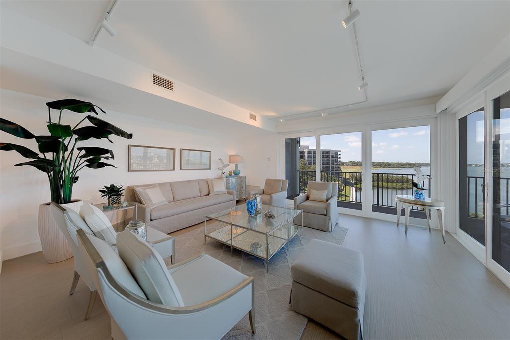 A bright living room features neutral furniture, a glass coffee table, and floor-to-ceiling balcony doors — 8 BELLEVIEW BOULEVARD UNIT 507, BELLEAIR, FL