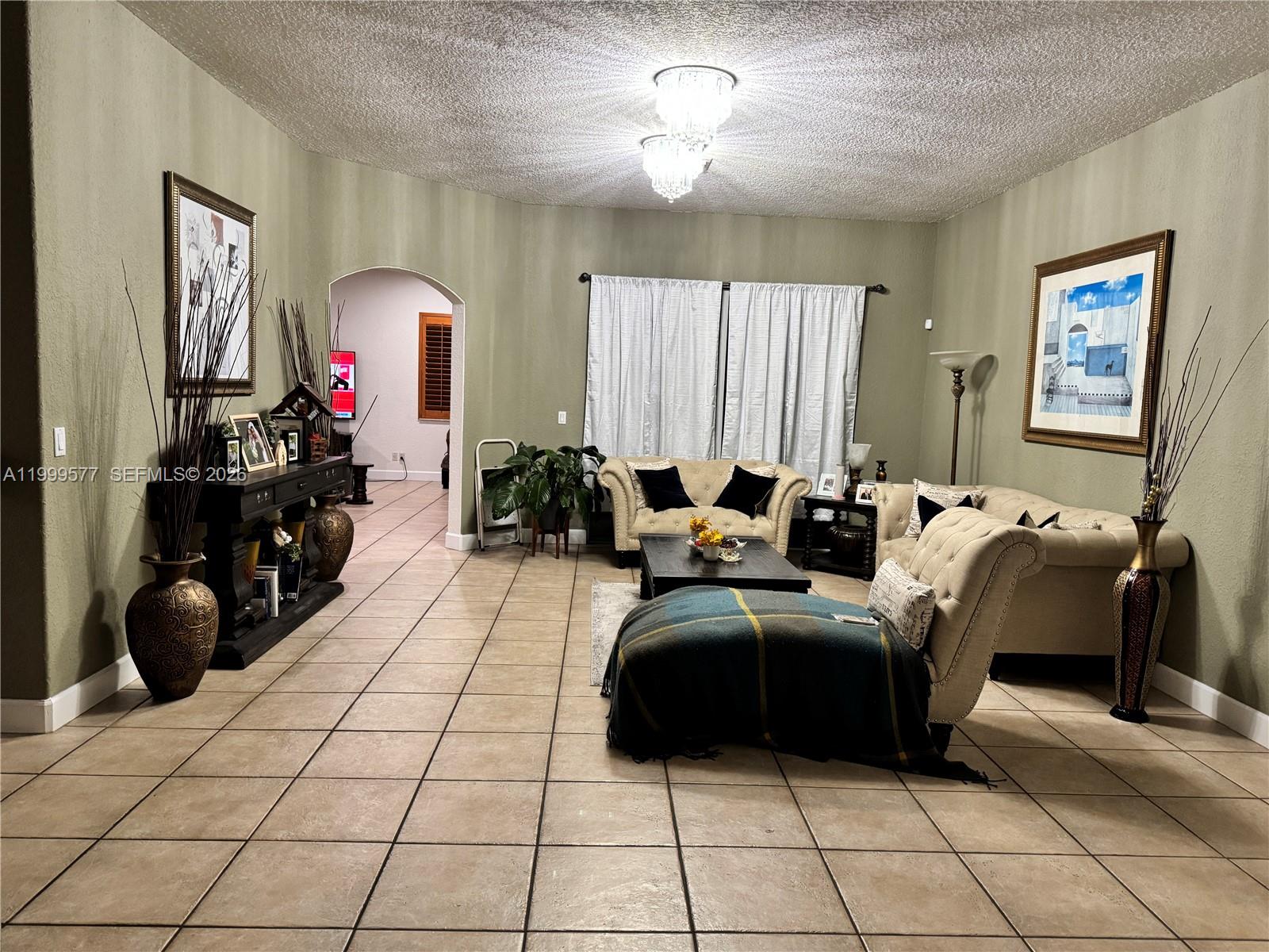 A living room features beige tufted sofas, tile flooring, and a decorative chandelier — 4000 SW 145th Ave, Miramar FL 33027, MIRAMAR, FL
