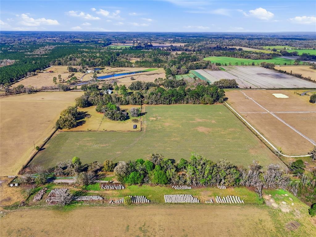 An aerial view shows a large, open pasture with a house, trees, and hay bales — TBD NW COUNTY ROAD 239, ALACHUA, FL