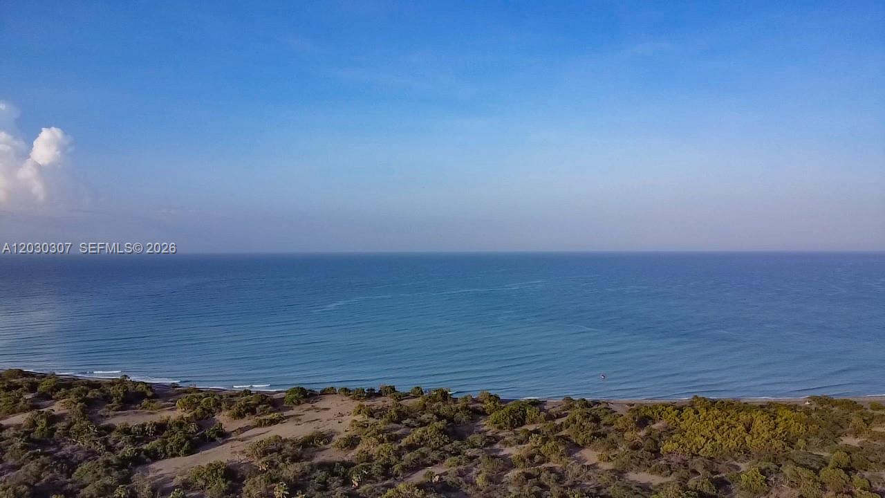 An aerial view shows a sandy beach meeting the ocean under a clear blue sky — Hwy 510, NA, NA