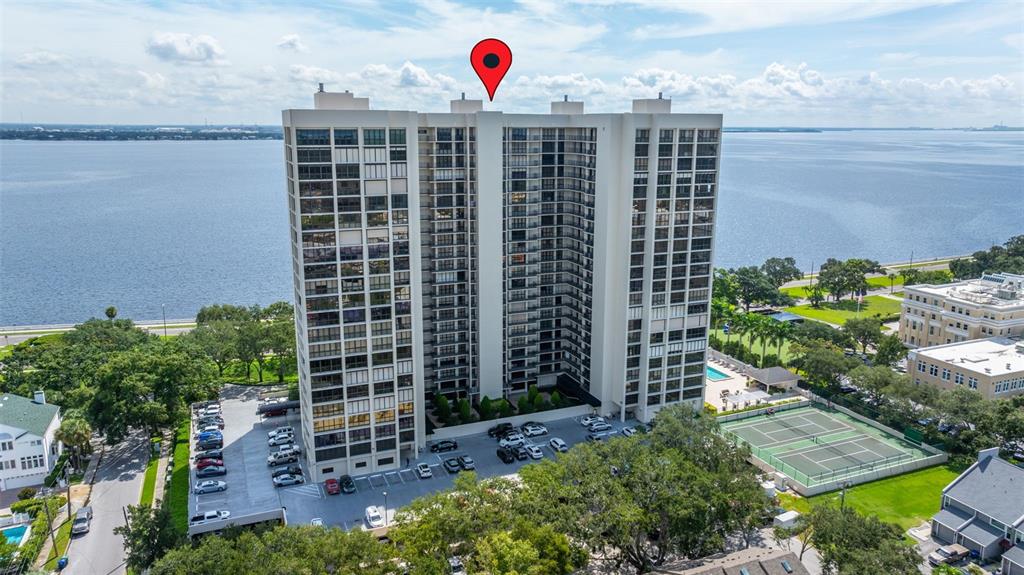 An aerial view of a tall residential building with a tennis court and waterfront views — 3301 BAYSHORE BOULEVARD UNIT 1510A, TAMPA, FL
