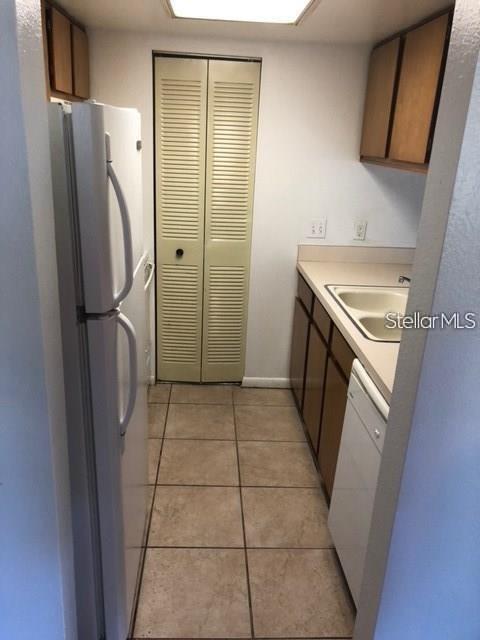 A galley kitchen features white appliances, light-colored cabinets, and tan tile flooring — 4922 W GANDY BOULEVARD UNIT 102, TAMPA, FL
