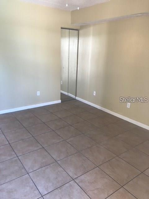 An empty room features beige walls, large square floor tiles, and a mirrored closet door — 4922 W GANDY BOULEVARD UNIT 102, TAMPA, FL