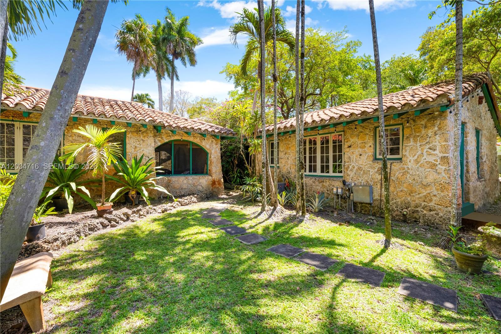 A stone-walled house with a tile roof sits beside a grassy yard with palm trees — 1301 Milan Ave, Coral Gables FL 33134, CORAL GABLES, FL