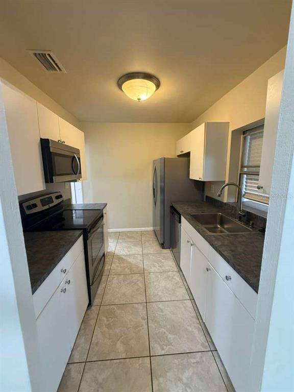 A galley kitchen features white cabinets, dark countertops, stainless steel appliances, and tiled flooring — 22189 LARAMORE AVENUE, PORT CHARLOTTE, FL