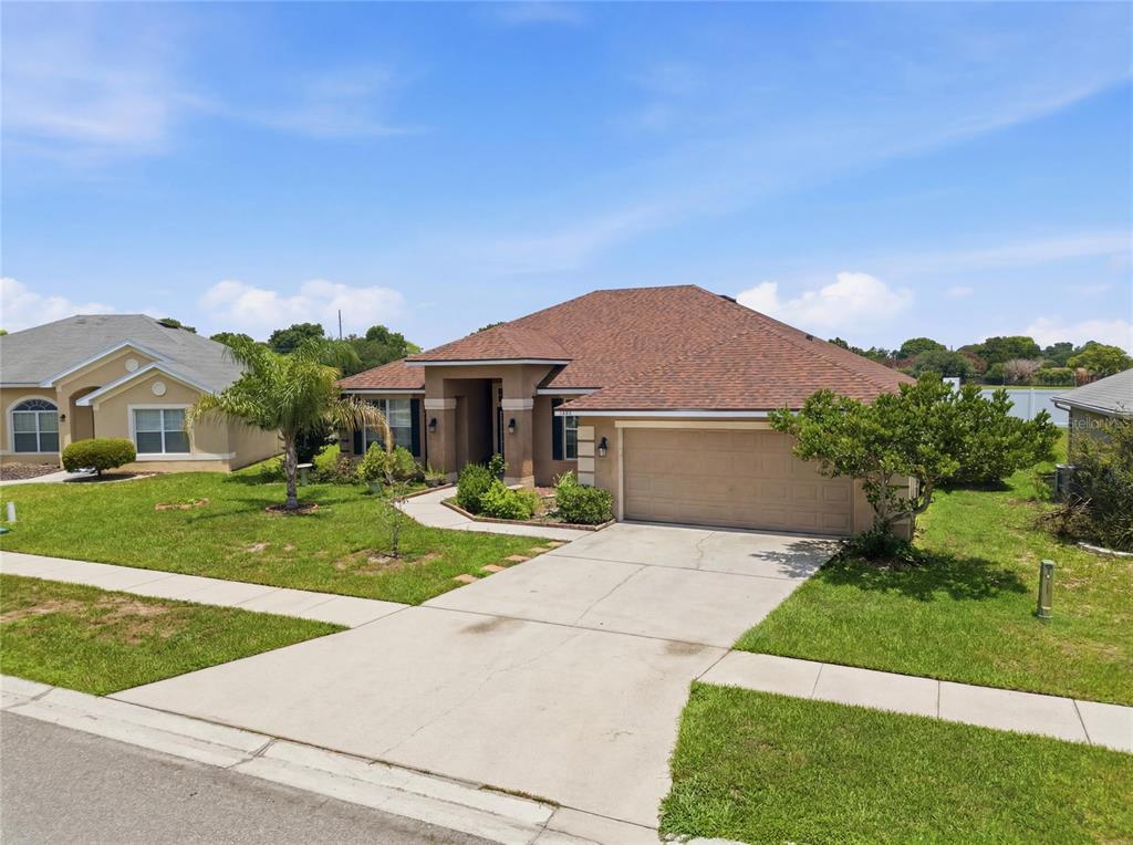 A single-story suburban house with a tan stucco exterior, brown roof, and two-car garage — 1097 NORMANDY HEIGHTS CIRCLE, WINTER HAVEN, FL