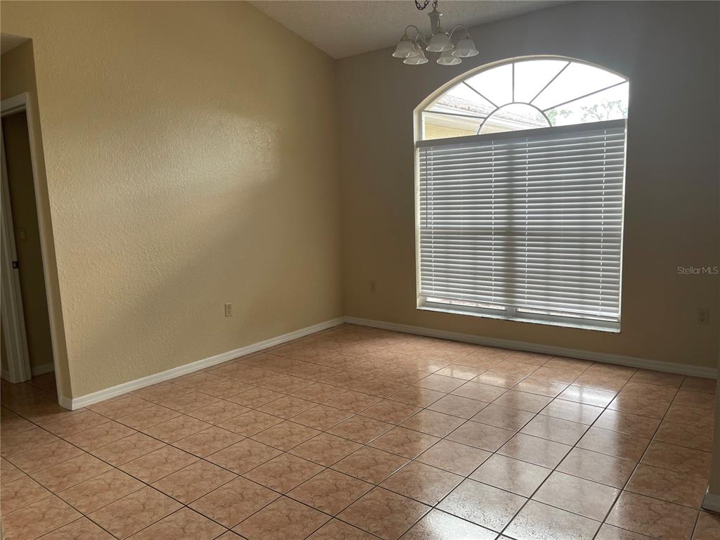 An empty room features tan tile flooring, beige walls, and a large arched window — 11018 AUDIE BROOK DRIVE, SPRING HILL, FL