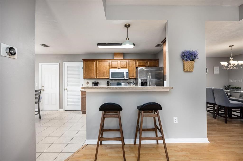 A kitchen with wood cabinets and stainless steel appliances overlooks a dining area with stools — 1608 NE 45TH PLACE, GAINESVILLE, FL