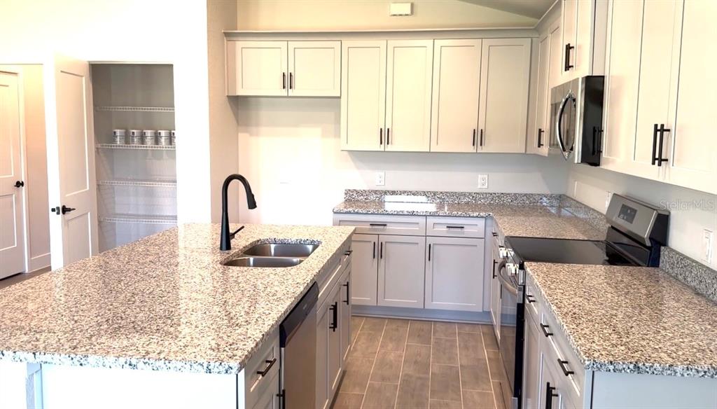 A kitchen features light gray cabinets, granite countertops, a center island, and stainless steel appliances — 12132 BACCHUS ROAD, PORT CHARLOTTE, FL