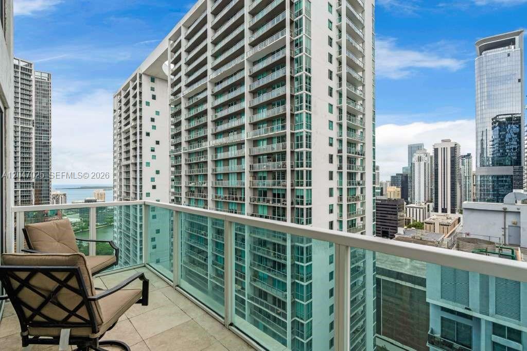 A high-rise balcony with a chair overlooks a dense urban skyline and nearby skyscrapers — 41 SE 5th St # 1702, Miami FL 33131, MIAMI, FL