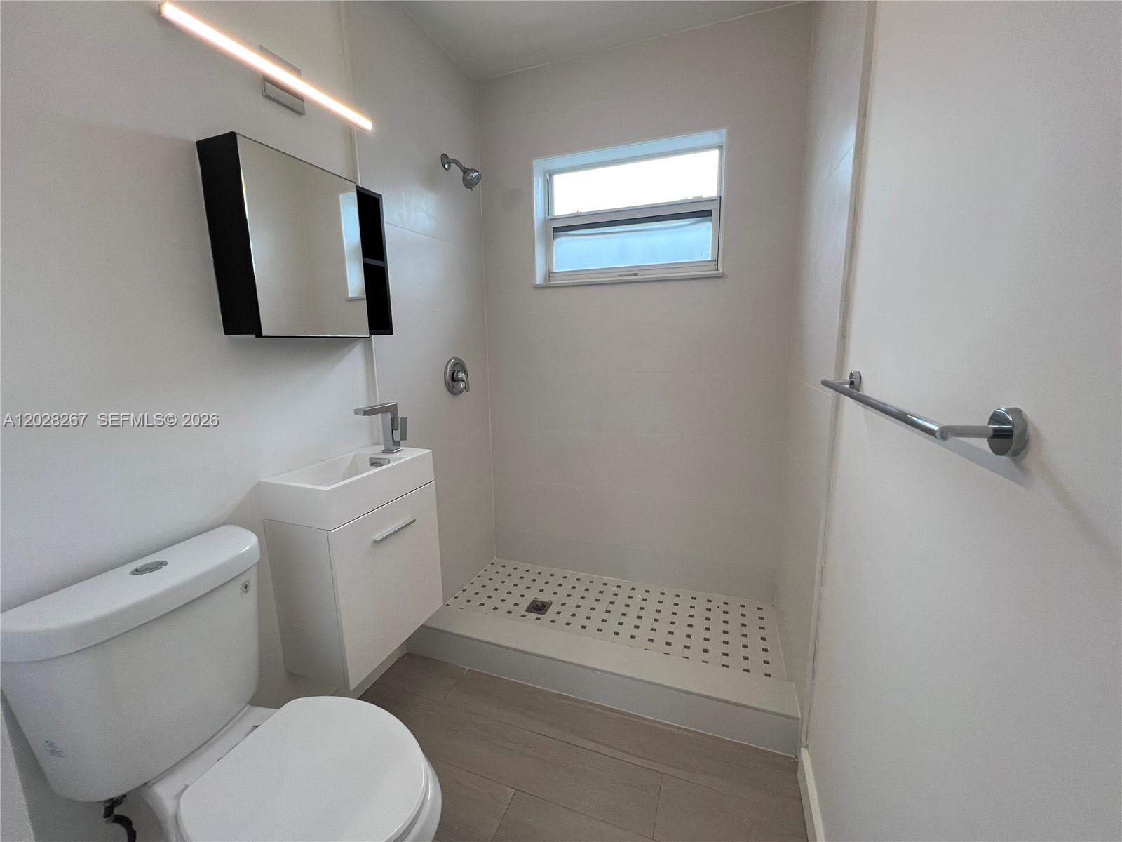 A small bathroom features a white toilet, a wall-mounted vanity, and a tiled shower stall — 7035 NE 4th Ct # 3, Miami FL 33138, MIAMI, FL