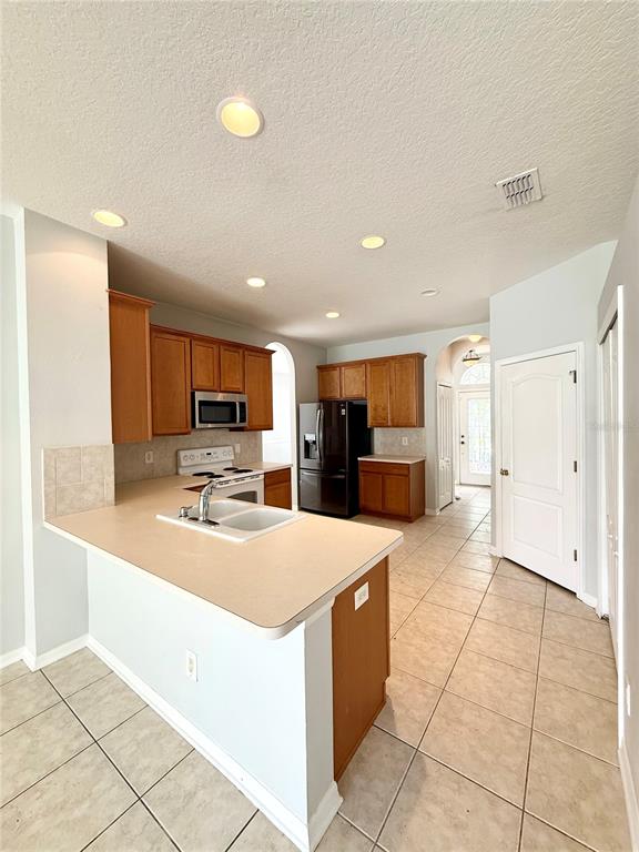 A kitchen features wood cabinets, beige countertops, a black refrigerator, and light-colored tile flooring — 20216 STILL WIND DRIVE, TAMPA, FL