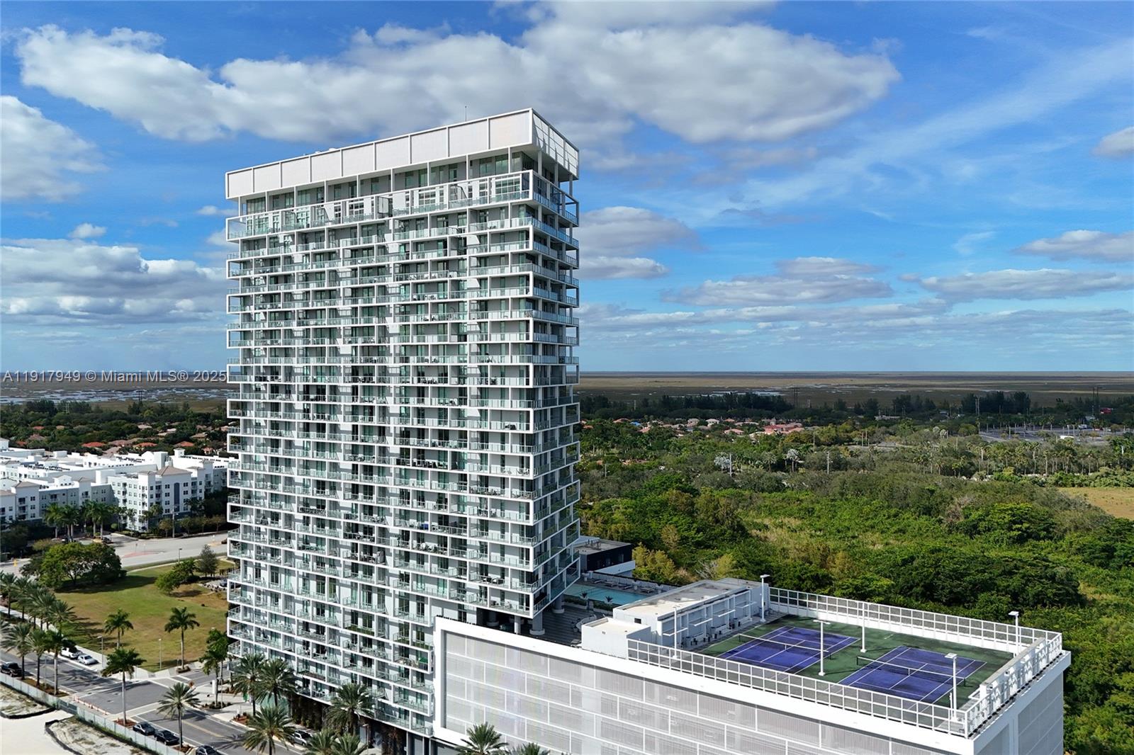 An aerial view shows a tall residential tower with balconies and a rooftop tennis court — 2000 Metropica Way # 306, Sunrise FL 33323, SUNRISE, FL