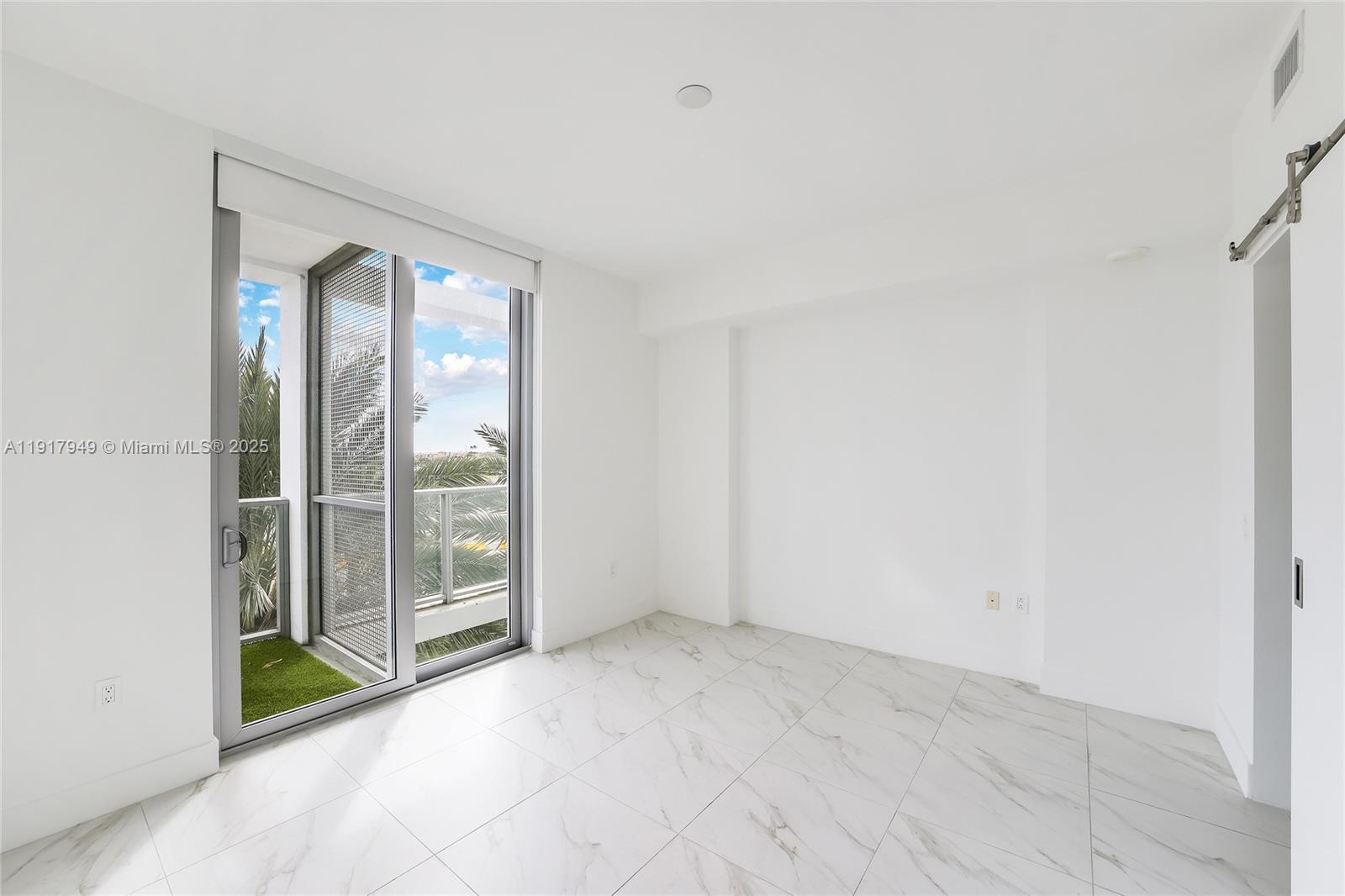 A bright, empty room features white walls, marble-patterned tile flooring, and a sliding glass door — 2000 Metropica Way # 306, Sunrise FL 33323, SUNRISE, FL