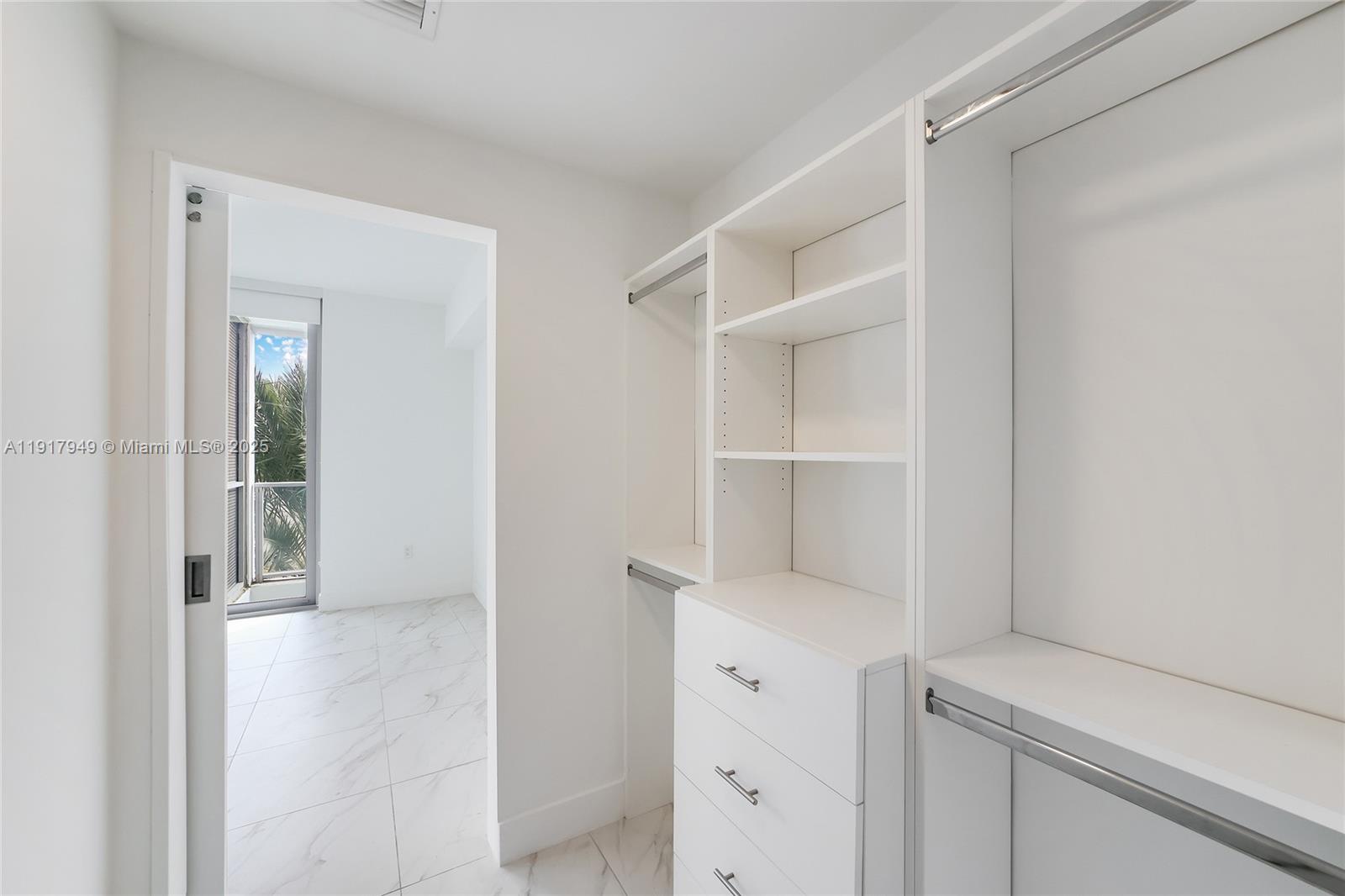 A walk-in closet with white shelving and drawers leads to a room with balcony access — 2000 Metropica Way # 306, Sunrise FL 33323, SUNRISE, FL