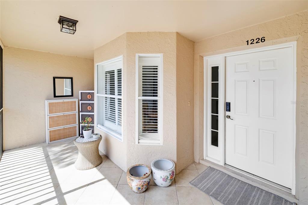 A covered entryway features a white front door, tiled flooring, and a small seating area — 5220 HYLAND HILLS AVENUE UNIT 1226, SARASOTA, FL