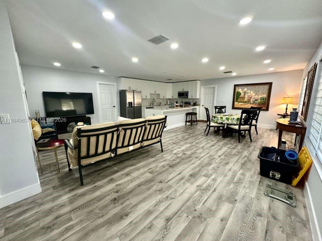 An open-concept living and dining area features light wood-look flooring and recessed ceiling lighting — 628 SW 6th Ave, Hallandale Beach FL 33009, HALLANDALE BEACH, FL