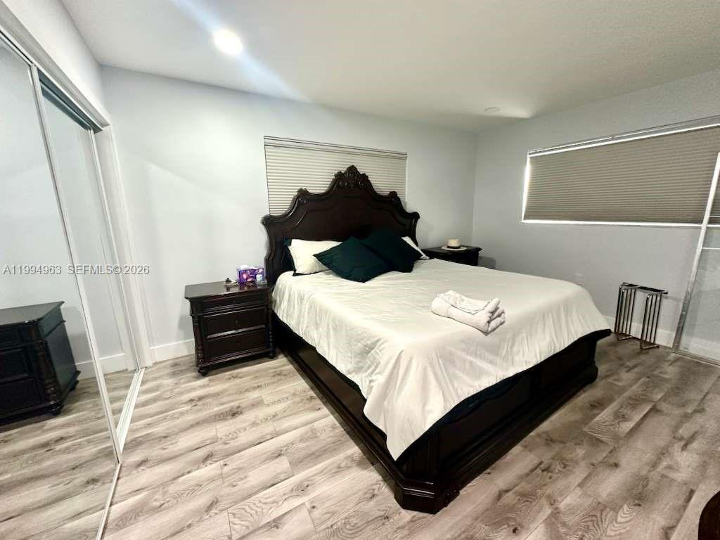 A bedroom features a dark wood bed frame, light wood-look flooring, and white walls — 628 SW 6th Ave, Hallandale Beach FL 33009, HALLANDALE BEACH, FL