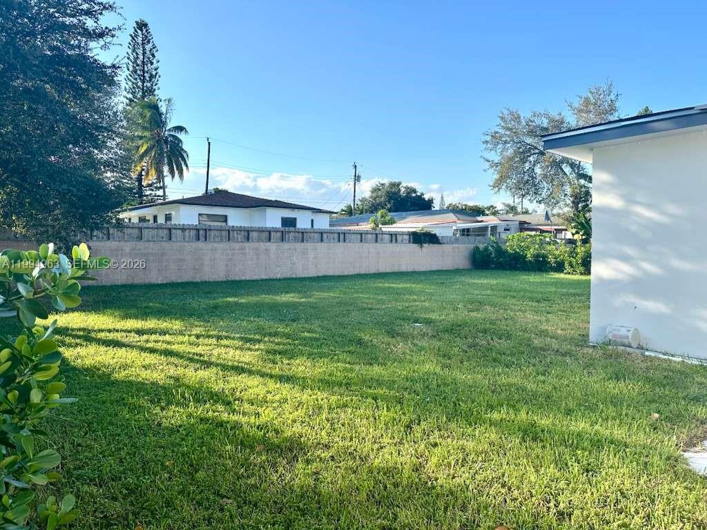 A grassy backyard features a tall concrete wall and a white house exterior — 628 SW 6th Ave, Hallandale Beach FL 33009, HALLANDALE BEACH, FL