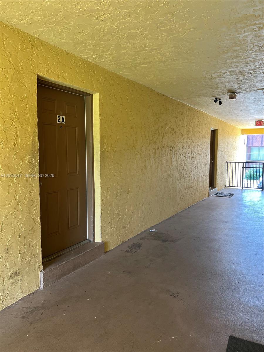 An exterior apartment hallway with yellow textured walls, a brown door labeled 2A, and concrete flooring — 2916 NW 55th Ave # 2A, Lauderhill FL 33313, LAUDERHILL, FL