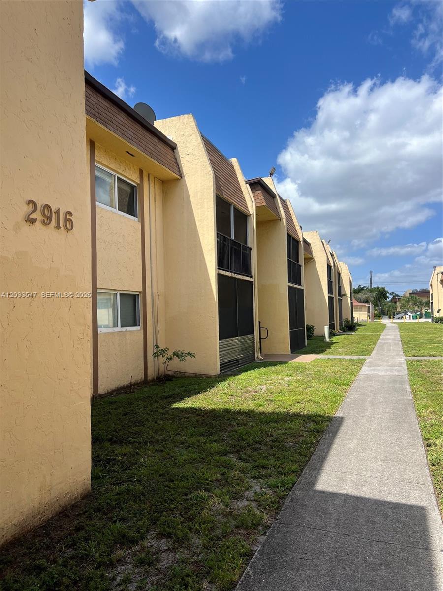 A multi-unit, two-story yellow stucco apartment building features screened balconies and a concrete walkway — 2916 NW 55th Ave # 2A, Lauderhill FL 33313, LAUDERHILL, FL