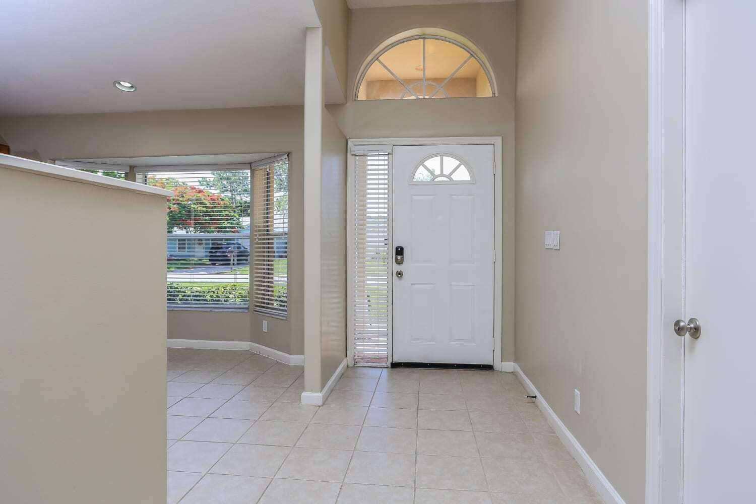 An entryway with tile flooring, a white front door, and a large arched transom window — JUPITER, FL