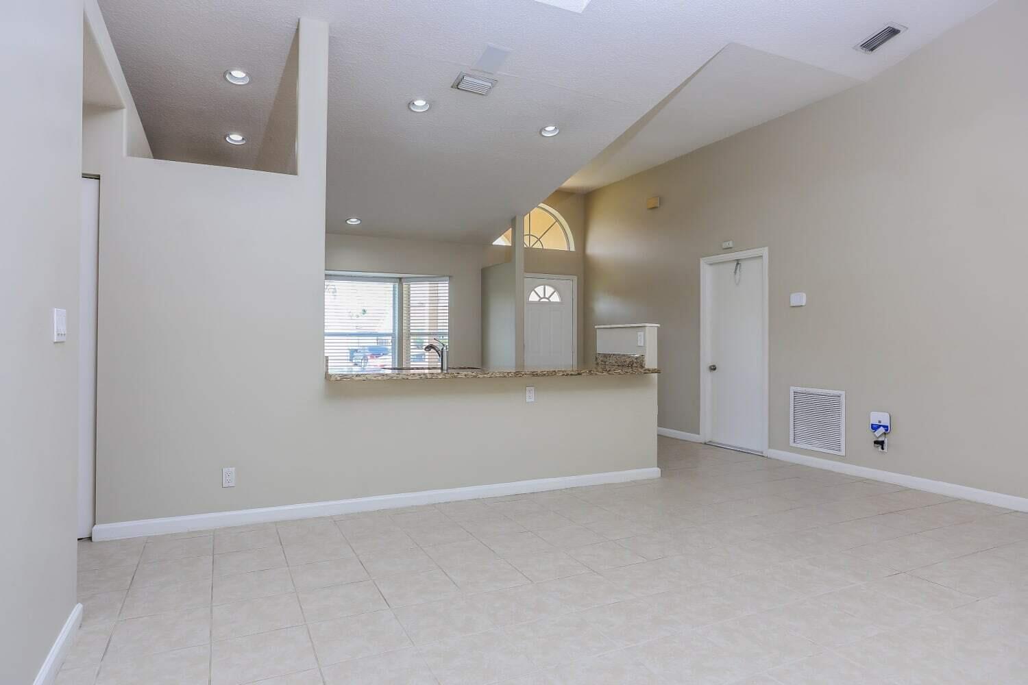 An open-concept living area features tile flooring, a kitchen breakfast bar, and vaulted ceilings — JUPITER, FL