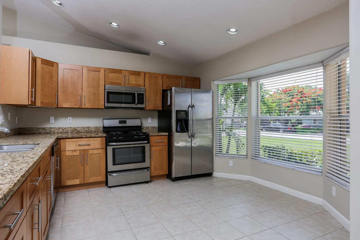 A kitchen with wood cabinets, granite countertops, stainless steel appliances, and a large bay window — JUPITER, FL
