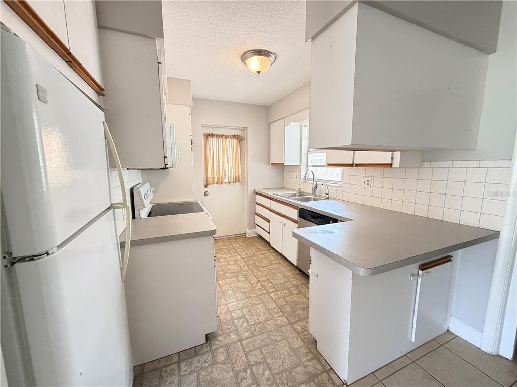 A kitchen features white cabinets, gray countertops, a white refrigerator, and a tiled backsplash — 3842 HAWKEYE CIRCLE, SARASOTA, FL