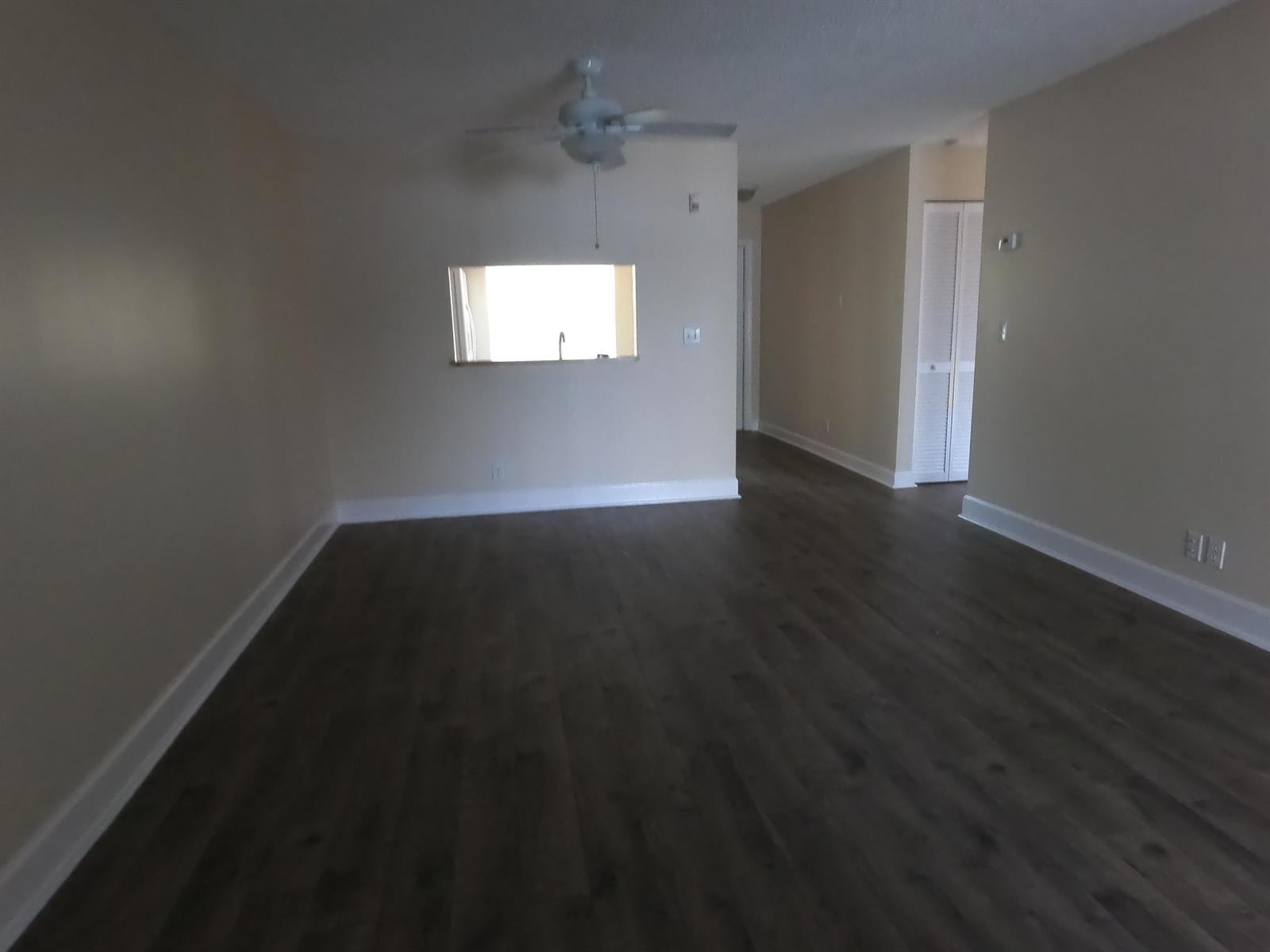 An empty living room features dark wood-look flooring, beige walls, and a ceiling fan — 16363 Water Way, Delray Beach FL 33484, DELRAY BEACH, FL