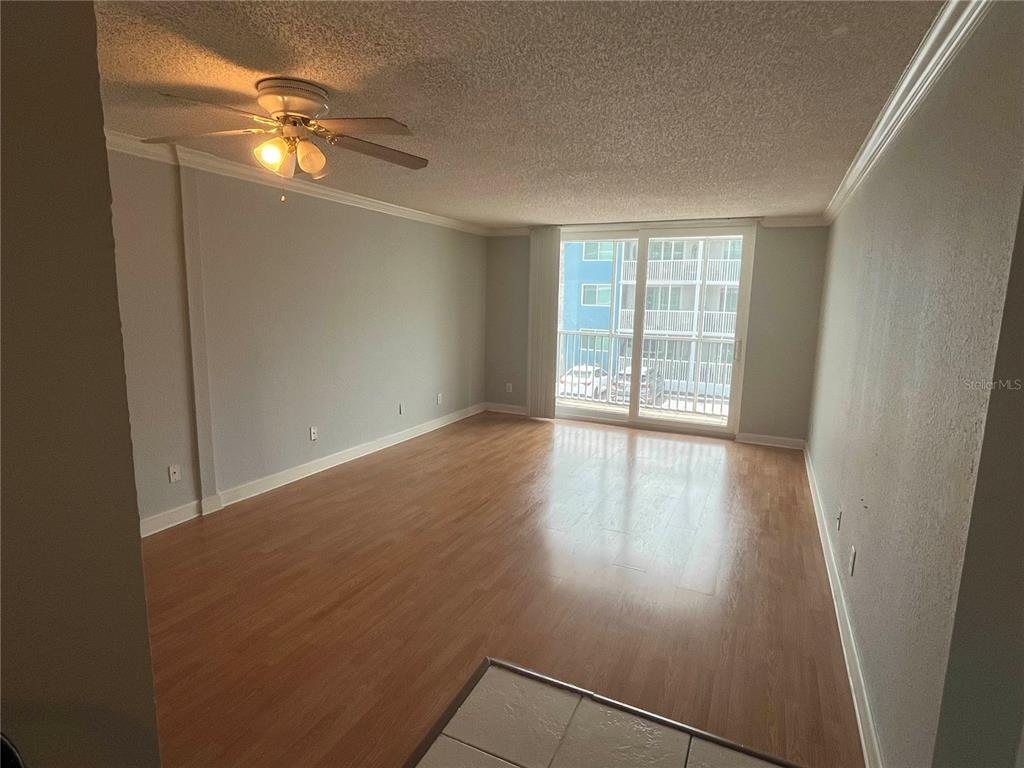 An empty living room with light wood-look flooring, a ceiling fan, and a sliding glass door — 2755 COCONUT BAY LN LANE UNIT 128, SARASOTA, FL