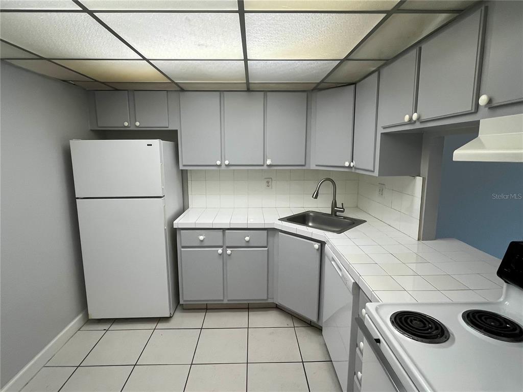 A kitchen features gray cabinets, white tiled countertops, a white refrigerator, and a drop ceiling — 2755 COCONUT BAY LN LANE UNIT 128, SARASOTA, FL