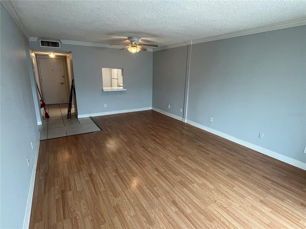 An empty living room features light wood-look flooring, light blue walls, and a ceiling fan — 2755 COCONUT BAY LN LANE UNIT 128, SARASOTA, FL
