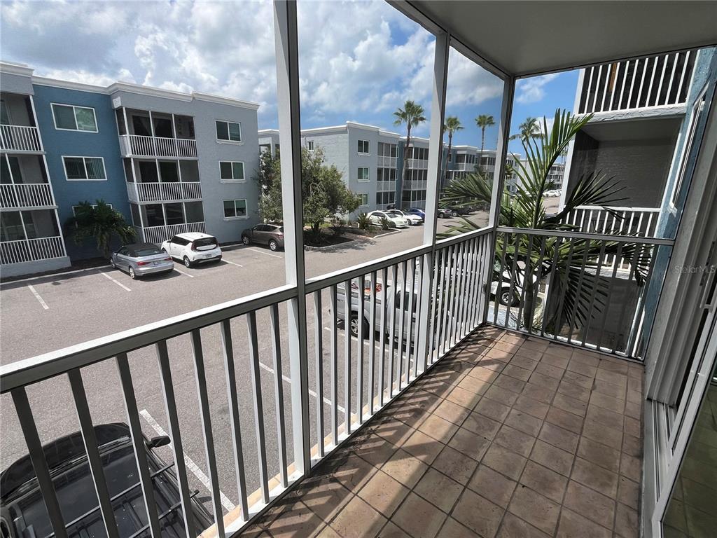 A screened-in balcony with tiled flooring overlooks a parking lot and apartment buildings — 2755 COCONUT BAY LN LANE UNIT 128, SARASOTA, FL
