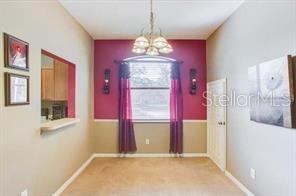 A dining room features a chandelier, a window with red curtains, and a pass-through opening — 6037 SCOTCHWOOD GLEN UNIT 8, ORLANDO, FL