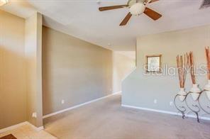 A carpeted living room features a ceiling fan and a staircase with decorative wall art — 6037 SCOTCHWOOD GLEN UNIT 8, ORLANDO, FL