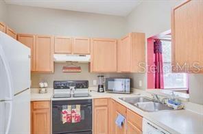 A kitchen features light wood cabinets, white appliances, and a double sink under a window — 6037 SCOTCHWOOD GLEN UNIT 8, ORLANDO, FL