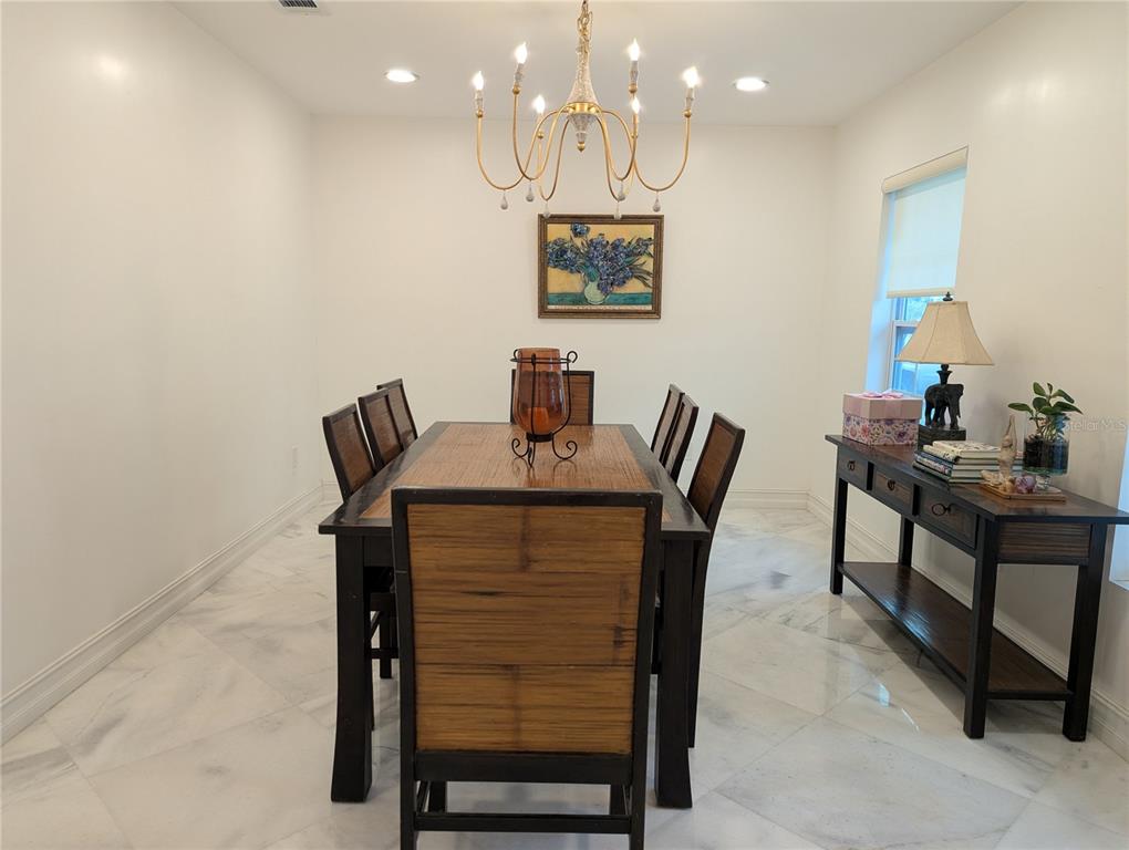 An open-concept living and dining area features white walls, marble-look tile flooring, and modern chandeliers — 974 PINELLI STREET, ORLANDO, FL