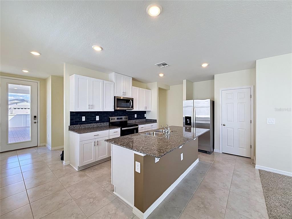 A kitchen features white cabinets, granite countertops, a center island, and stainless steel appliances — 520 KENNEDY DRIVE, LAKE ALFRED, FL