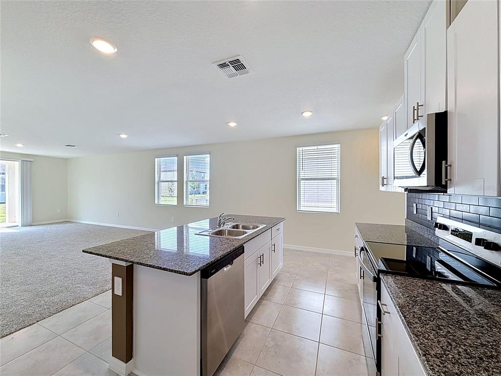 A kitchen with granite countertops, white cabinets, and stainless steel appliances overlooks a carpeted living area — 520 KENNEDY DRIVE, LAKE ALFRED, FL