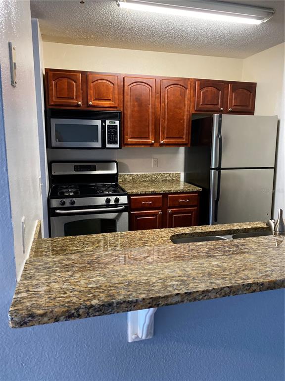 A kitchen features cherry wood cabinets, granite countertops, and stainless steel appliances — 2047 DIXIE BELLE DRIVE UNIT 2047H, ORLANDO, FL