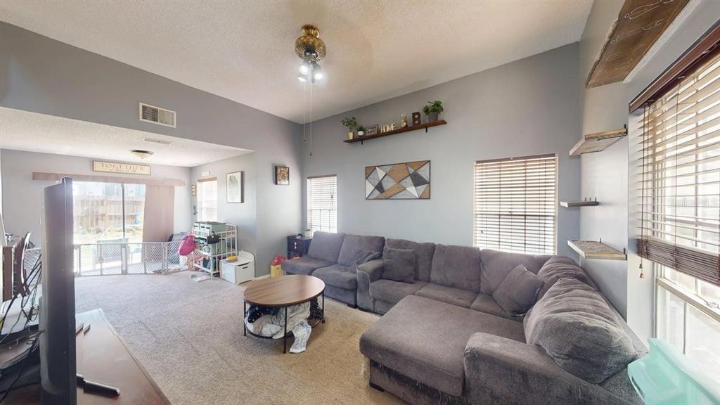 A living room features a large gray sectional sofa, carpeted floors, and high ceilings — 7508 OKEECHOBEE COURT, TAMPA, FL