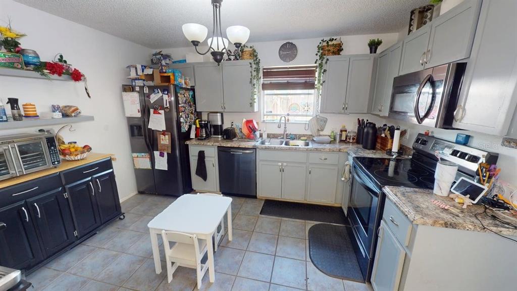 A kitchen features grey cabinets, stainless steel appliances, a small white table, and tiled flooring — 7508 OKEECHOBEE COURT, TAMPA, FL