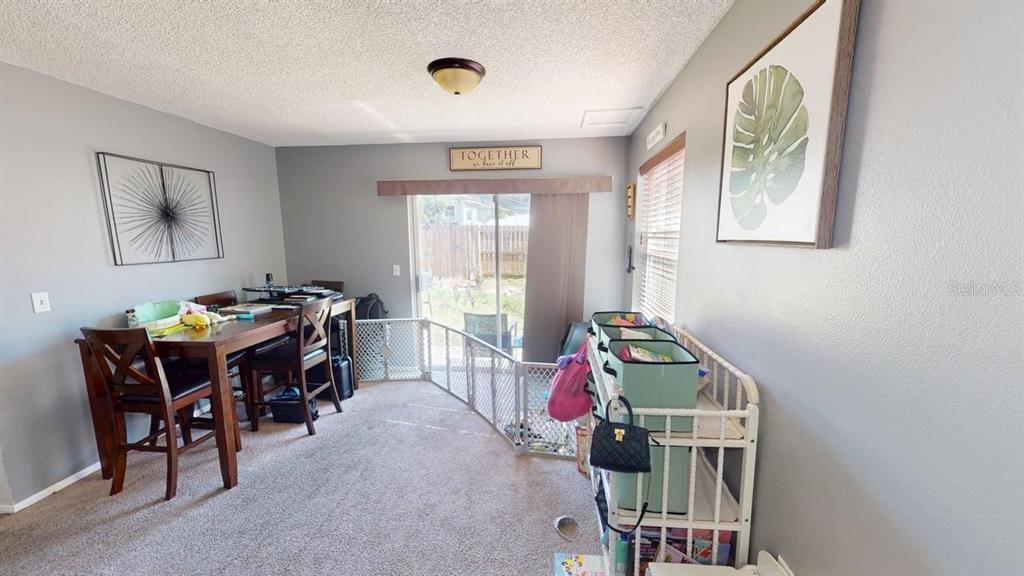 A dining area with carpeted floors, a sliding glass door, and a white baby gate — 7508 OKEECHOBEE COURT, TAMPA, FL